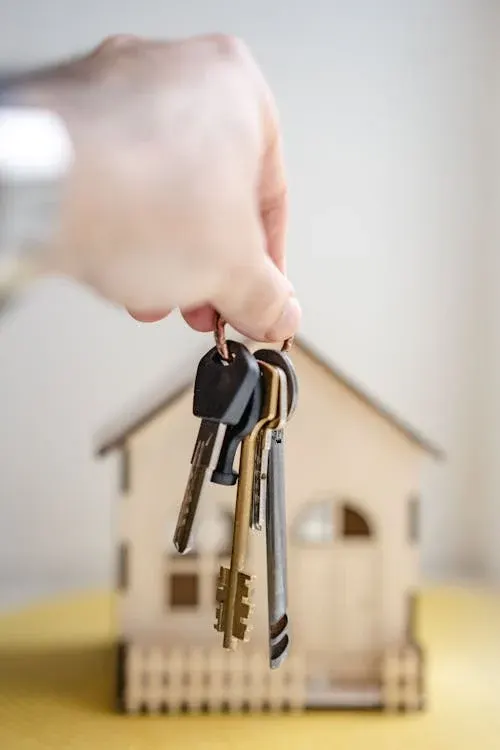 A hand holding a bunch of keys in front of a small wooden model house