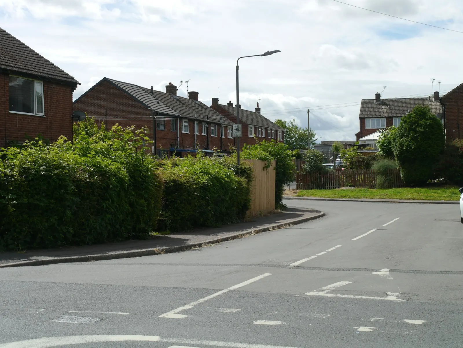 A quiet suburban street of brick semi-detached houses behind hedges