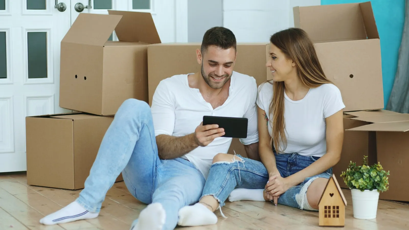 A couple sitting on the floor among cardboard boxes, looking at a tablet