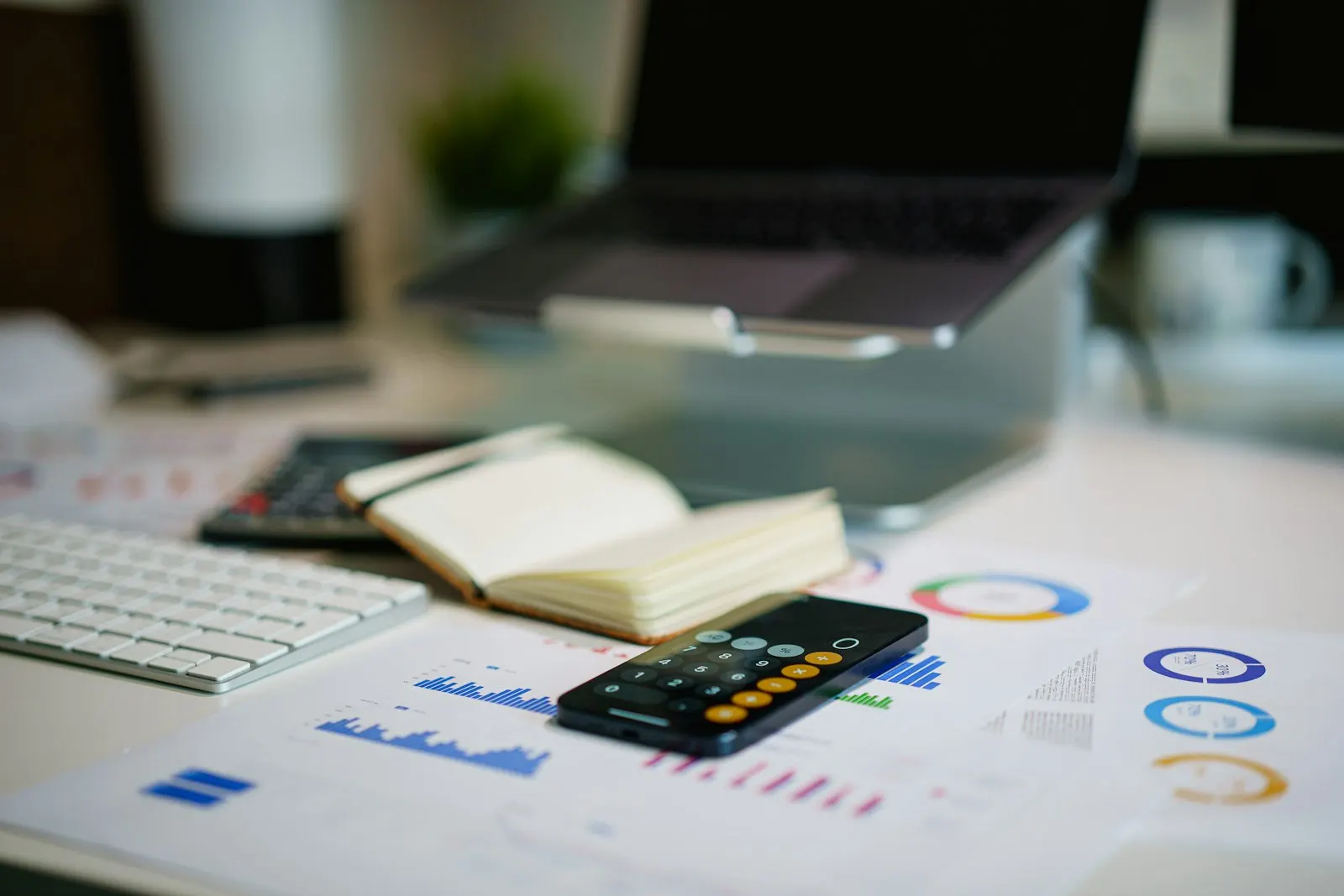 A desk with a laptop, calculator, notebook and printed charts