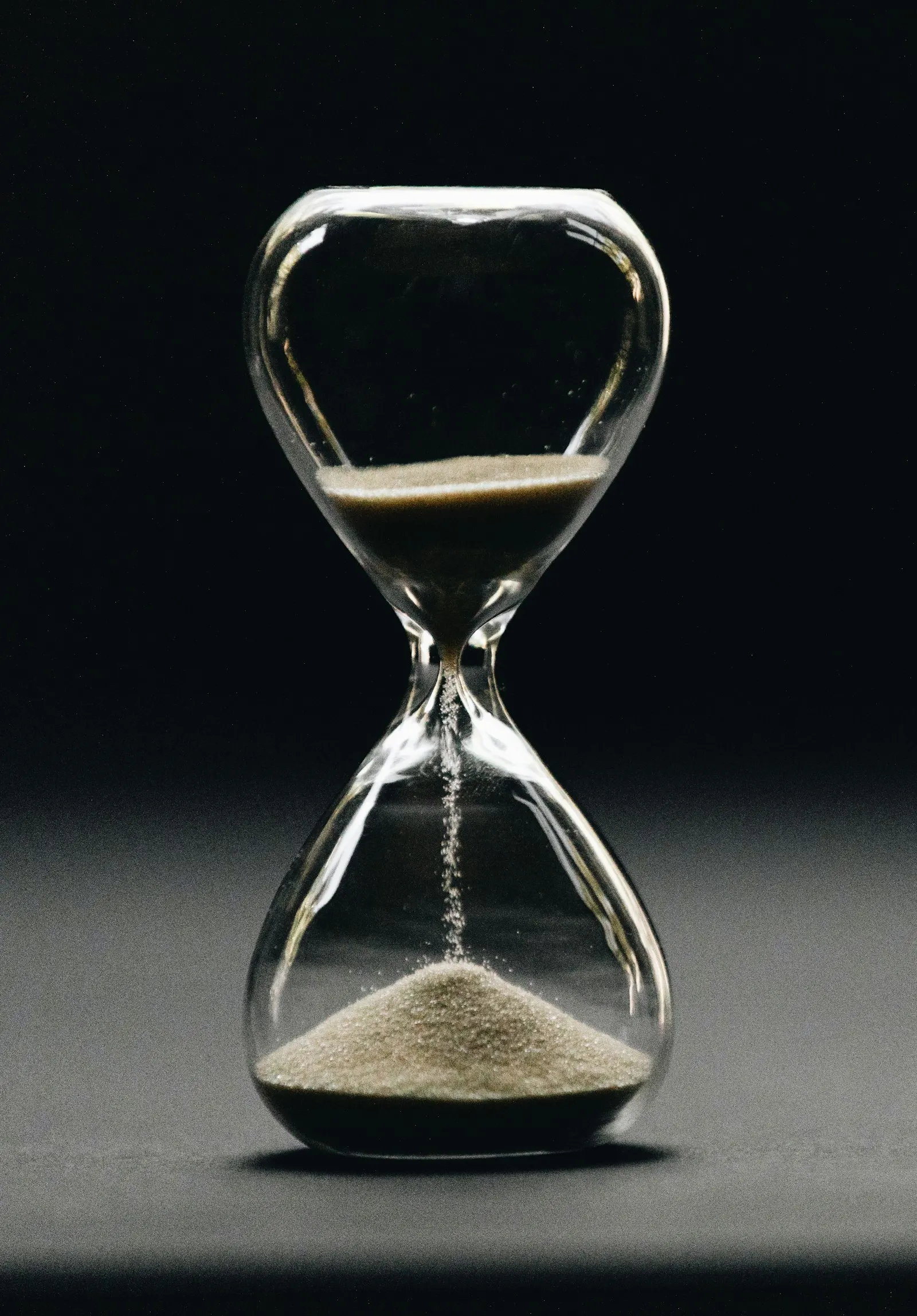 An hourglass with sand running through it against a dark background