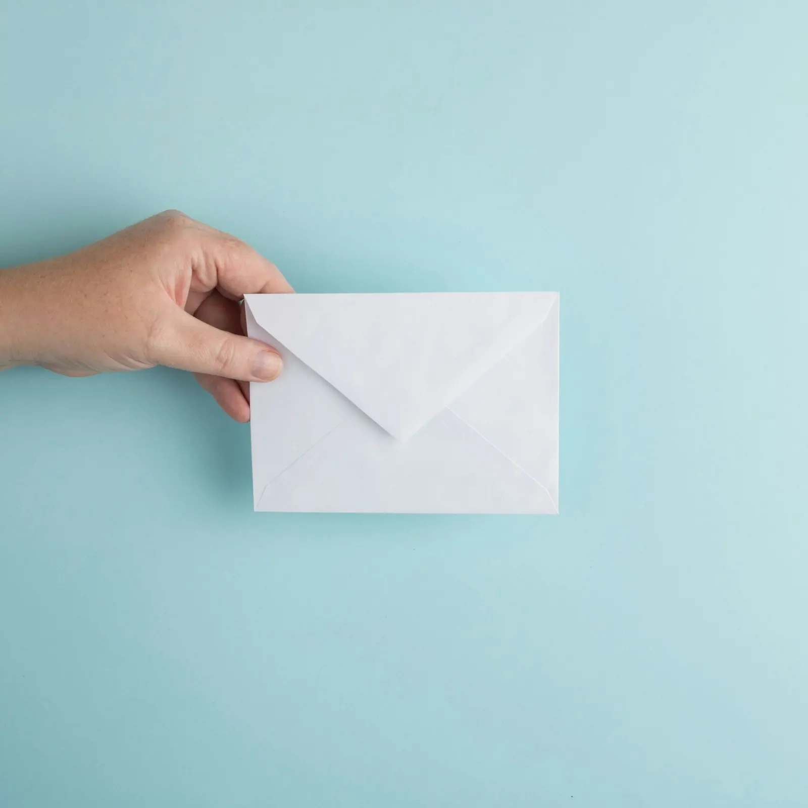 A hand holding a plain white envelope against a pale blue background