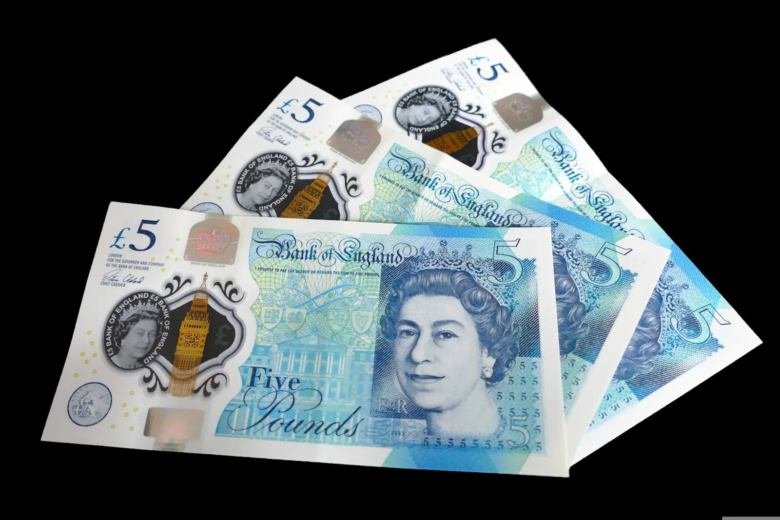 Several five-pound notes fanned out on a black surface