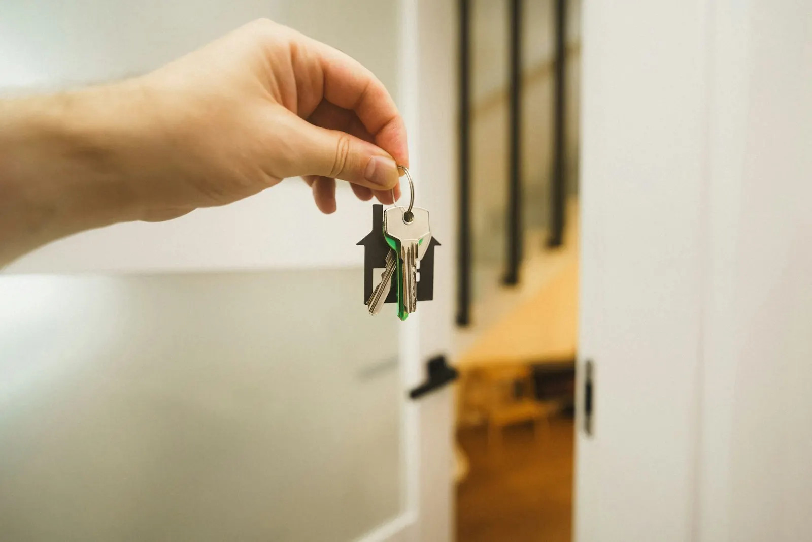 A hand holding keys with a house-shaped keyring beside an open door
